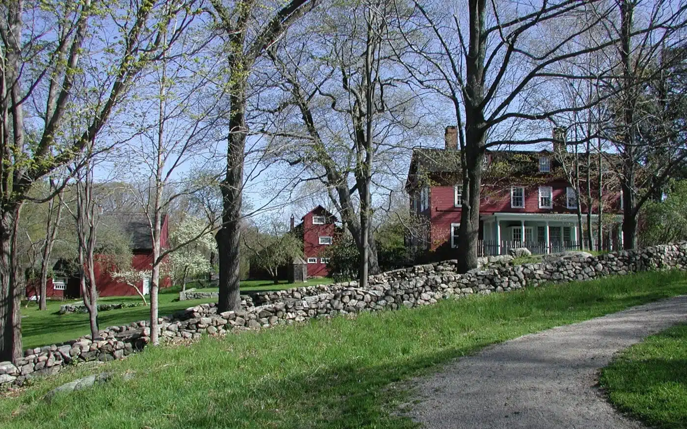 A red house and buildings behind a stone wall and some trees.