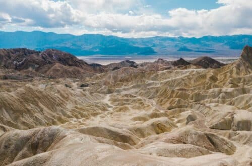 Sweeping view of Death Valley's rugged terrain with undulating hills and the Panamint Range in the distance, under a partly cloudy sky, highlighting the natural beauty that surrounds Death Valley Airbnbs and vacation rentals.