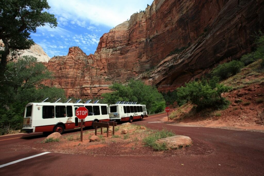 Zion Shuttle driving down the road surrounded by Zion's towering orange cliffs.  