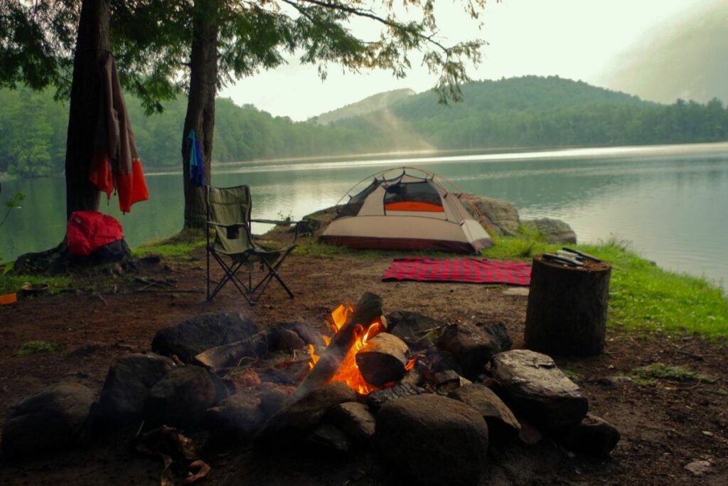 Campsite by the lake with a tent and campfire.