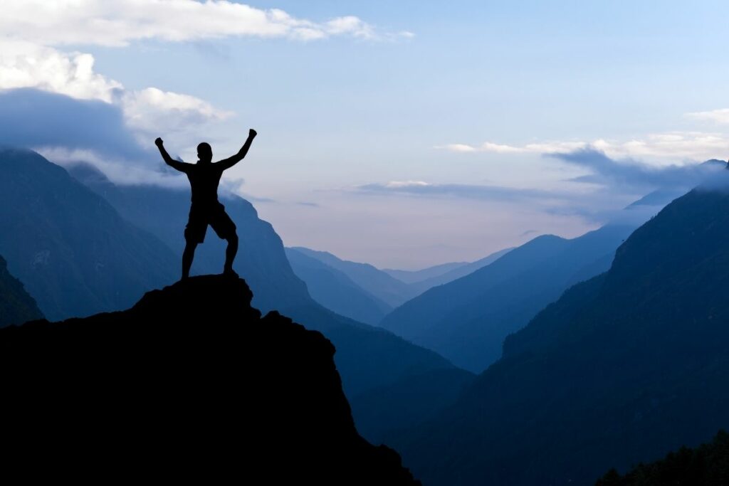 A hiker enjoying blue hour in the mountains with his arms raised. 