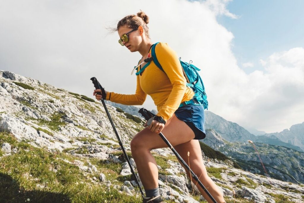 A women in a yellow shirt and trekking poles hiking up an incline