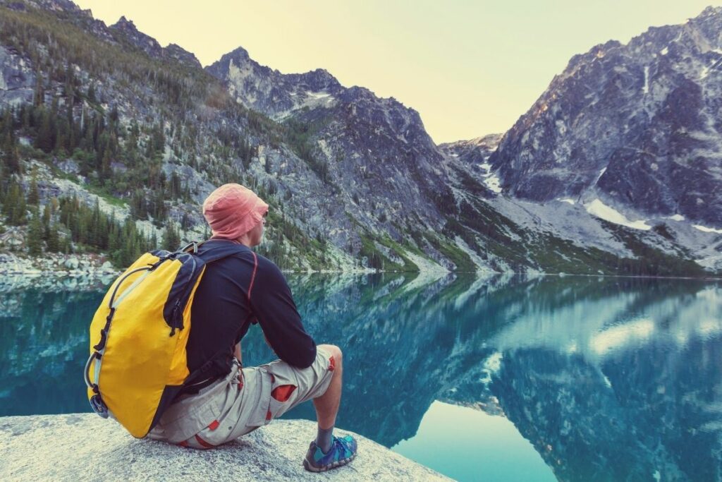 A man sitting by an alpine lake enjoying the mountain view. 