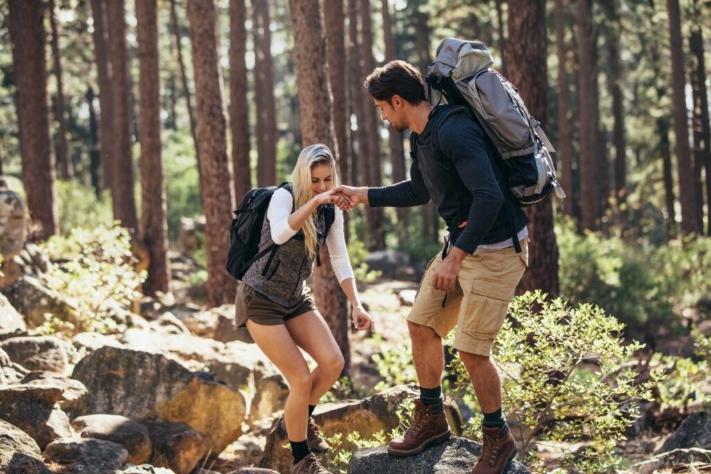 A man and woman hiking on some rocks.  The man is helping the woman up. 