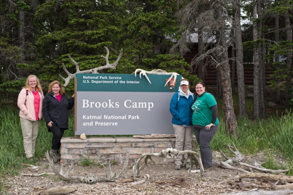 Four women standing with the Brooks Camp Sign. 