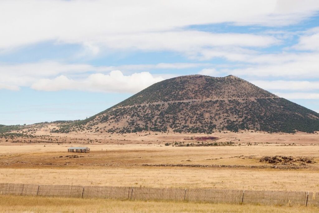 A cinder cone volcano next to a dry field