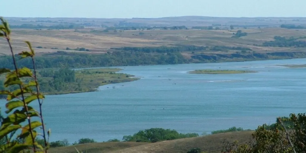 Look over the blue Missouri River with a couple of green islands and fields in the background. 