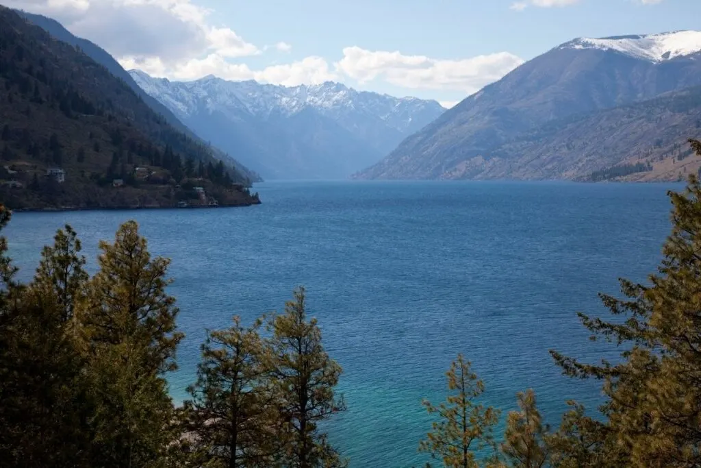 A blue mountain lake with snow capped mountains in the background.