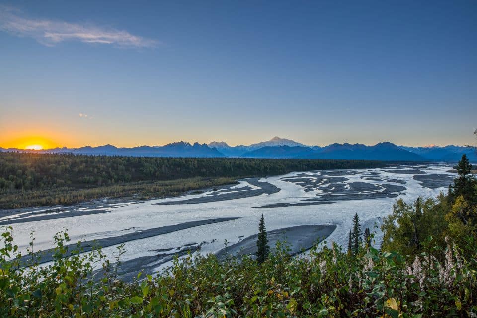 Sunset view over a braided river flowing through Denali National Park with a backdrop of the Alaska Range, highlighting the expansive, untouched wilderness.
