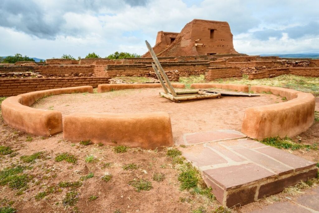 An ancient circular structure with adobe buildings in the background
