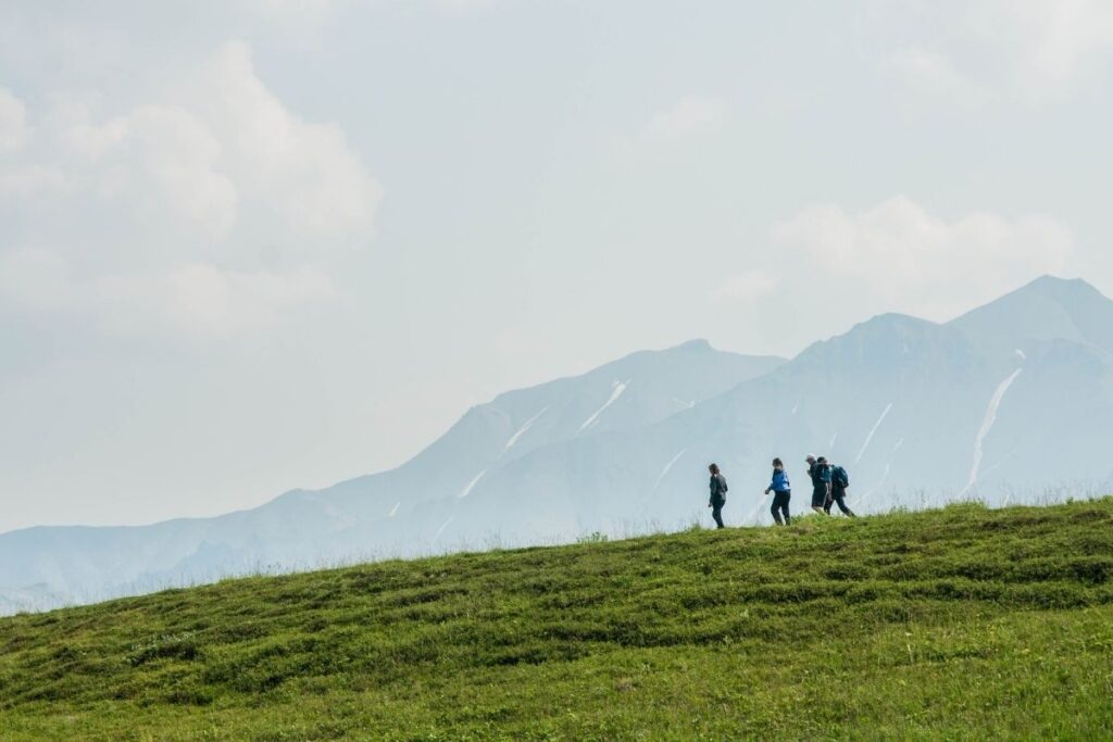 4 People hiking along a green ridge with mountains in the background