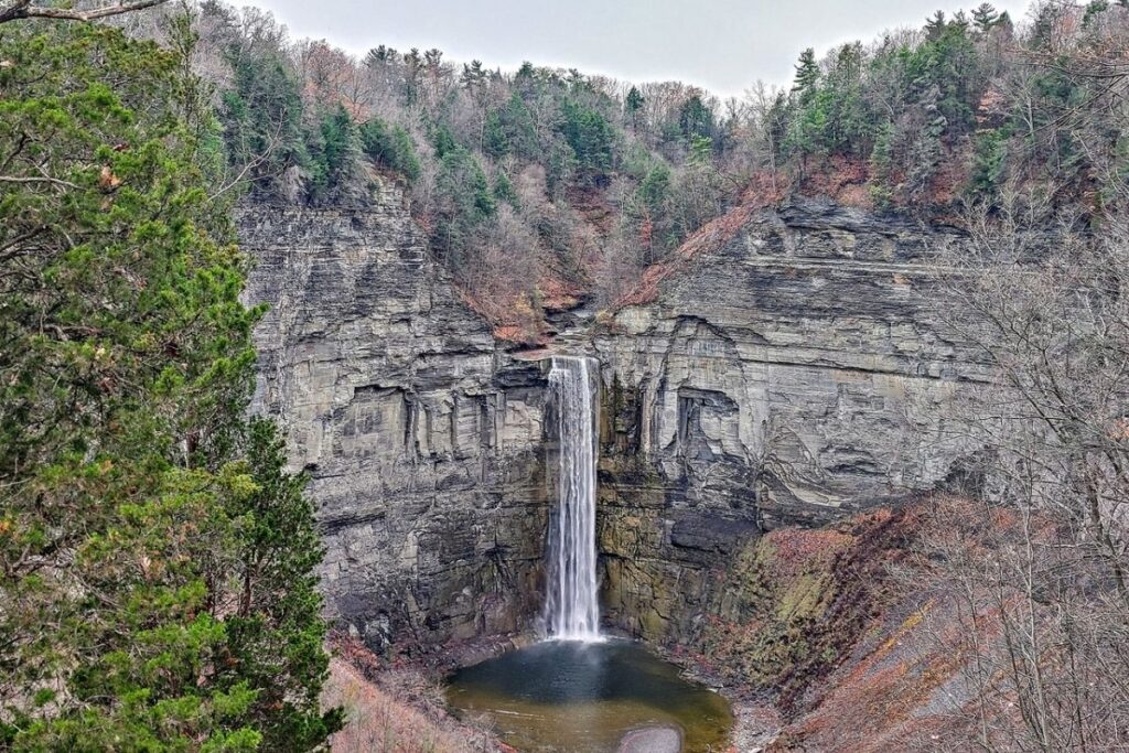 A tall waterfall goes down a grey cliff face