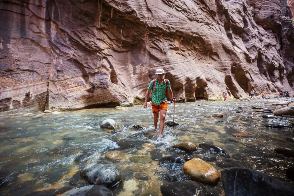 A of a hiker wades through the water of a canyon