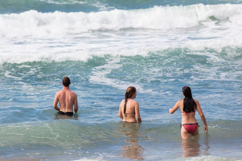 Two women and a man wading in the ocean