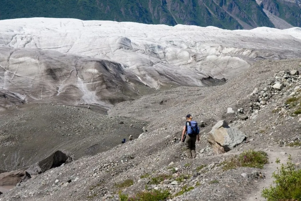 A hiker headsdown a rocky trail towards a glacier