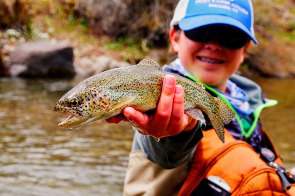 A kid holds up a trout he caught