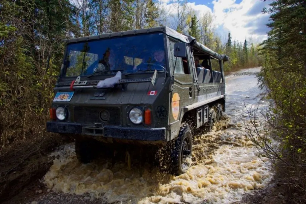 A military vehicle drives down the road covered in water. 