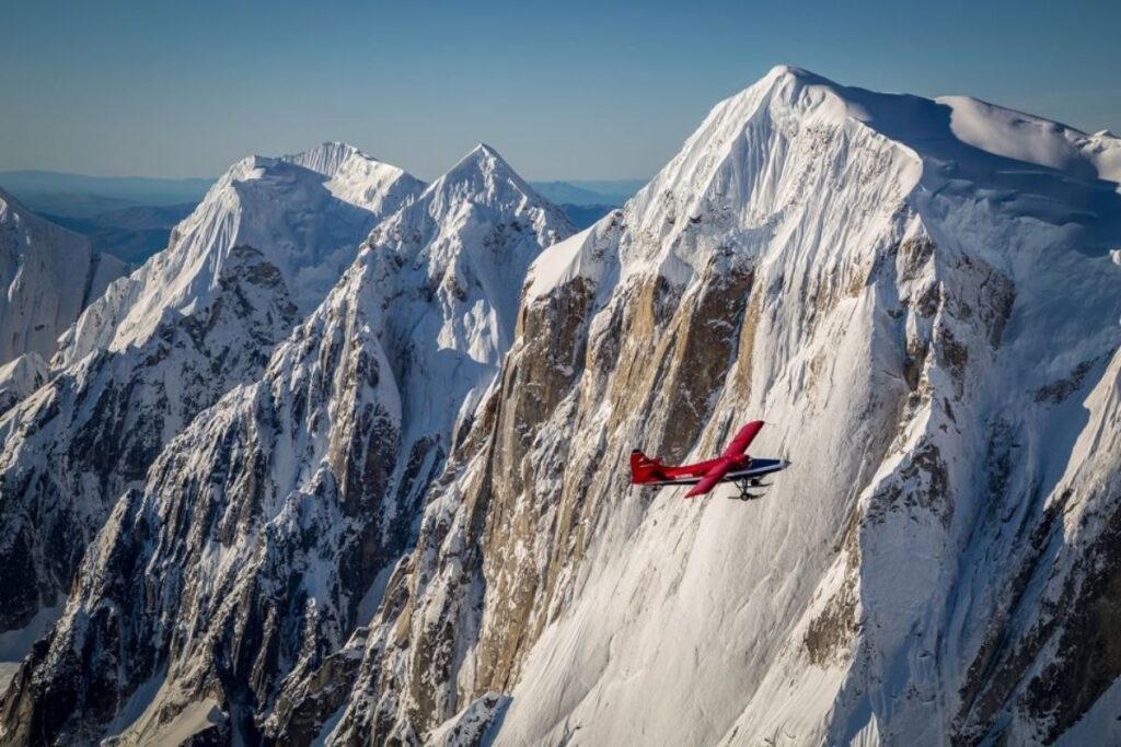 A red plane flying with mountains in the background