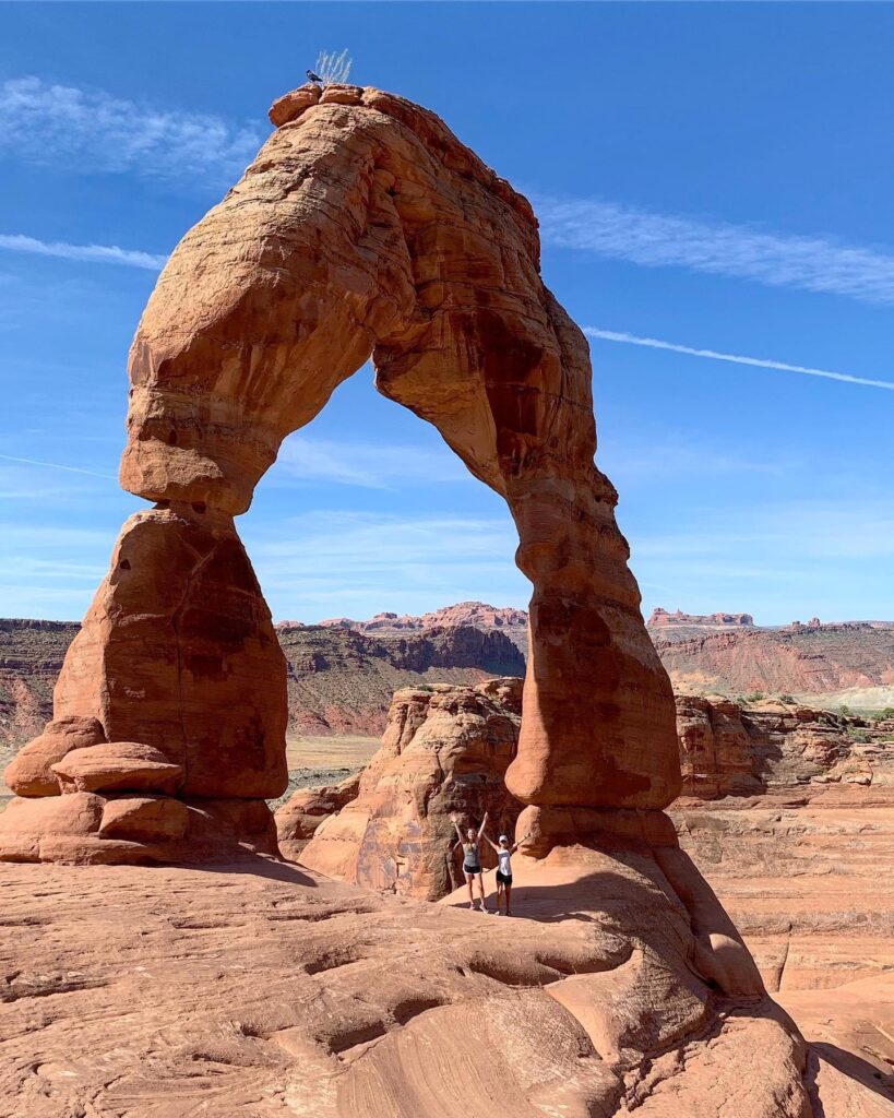 Two women stand under a Delicate Arch.  