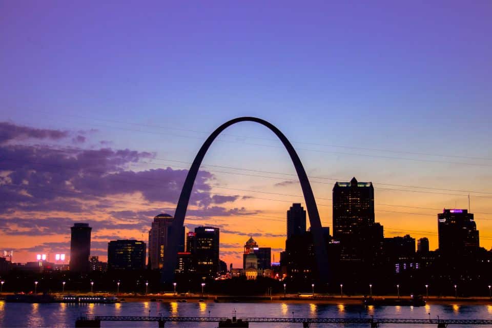A large arch in a city on the river at sunset