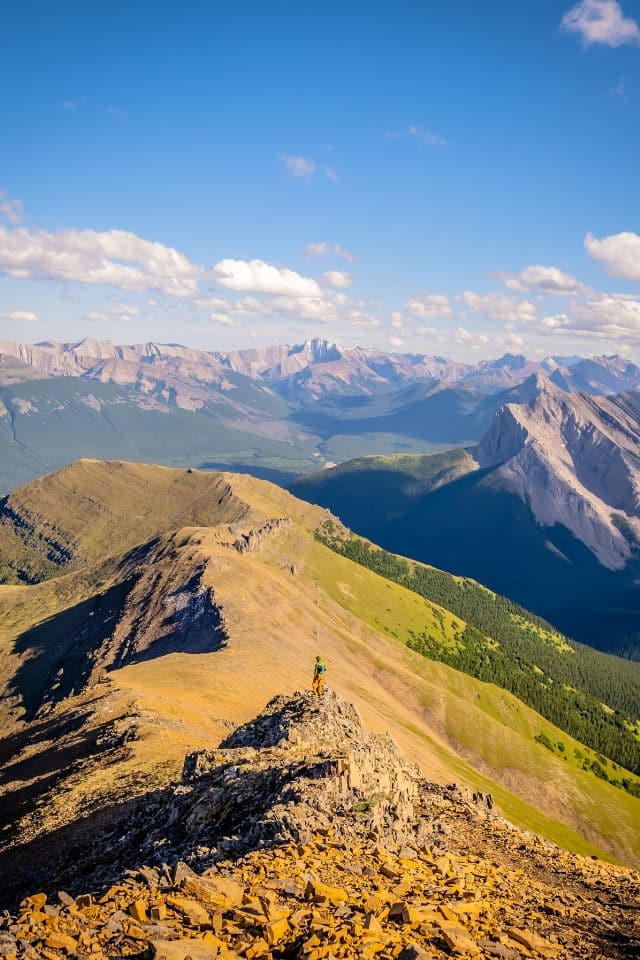 A lone hiker stands atop a rugged mountain ridge, with expansive views of jagged peaks, embodying 'Hiking Tips for Beginners' on reaching new heights.