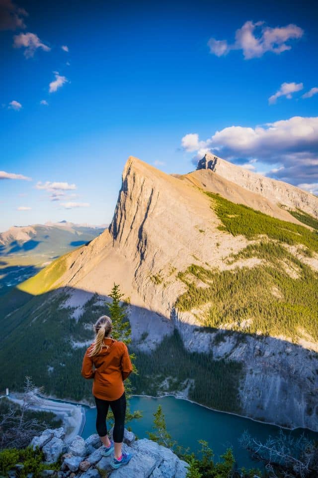 A hiker gazes out from a mountain ledge over a turquoise lake, exemplifying 'Hiking Tips for Beginners' on finding stunning viewpoints during a hike.