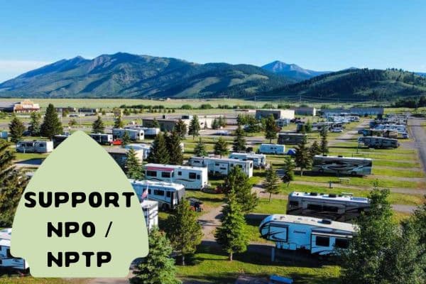 The image captures an expansive RV park set against a backdrop of rolling hills and mountains under a clear blue sky. Rows of parked recreational vehicles fill the park, suggesting a popular destination for travelers and campers.