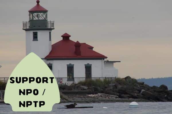 This image features a picturesque lighthouse with a red roof situated on a rocky shoreline under a cloudy sky. In the foreground, a green arrow-shaped sign reads "SUPPORT NPO / NPTP."