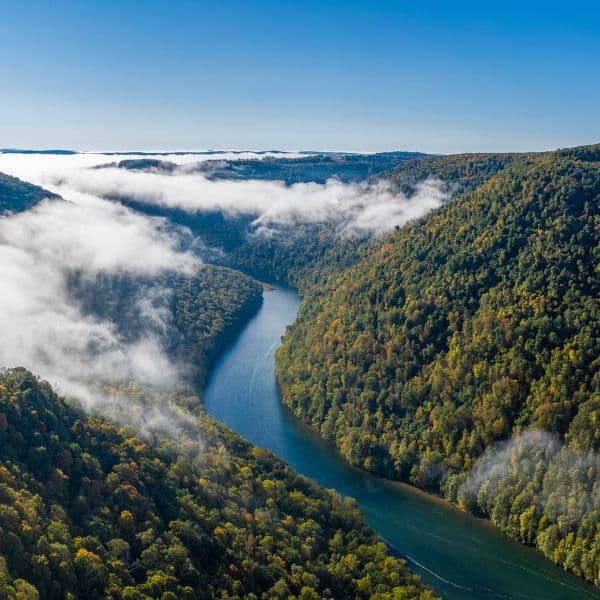 An aerial view of a river winding through a forested valley with clouds hanging low over the hills.