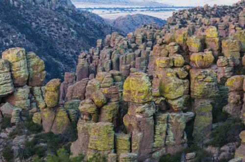 The image shows a rugged landscape featuring a dense cluster of towering rock formations, known as hoodoos, which are covered in a light greenish-yellow lichen.