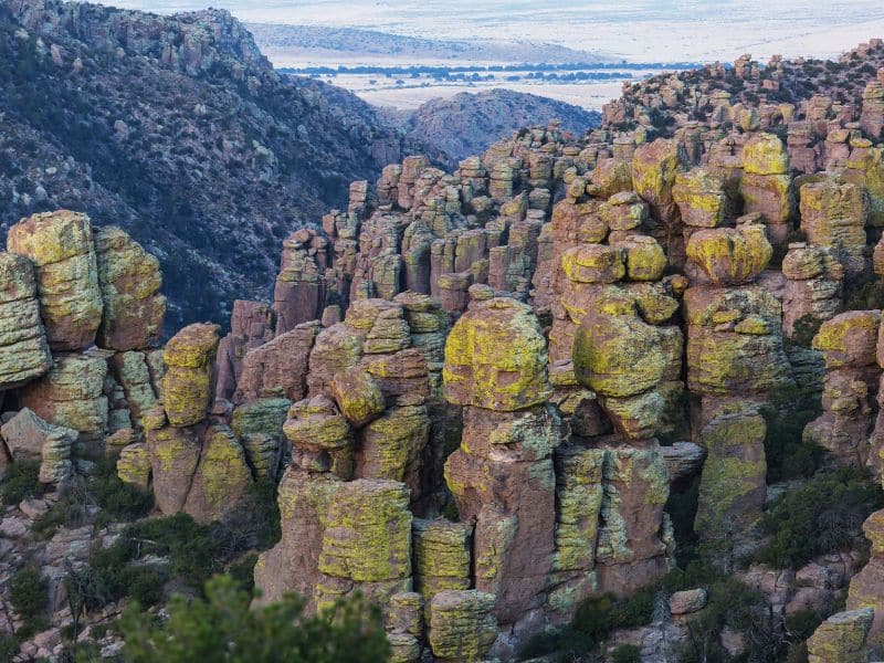 The image shows a rugged landscape featuring a dense cluster of towering rock formations, known as hoodoos, which are covered in a light greenish-yellow lichen.