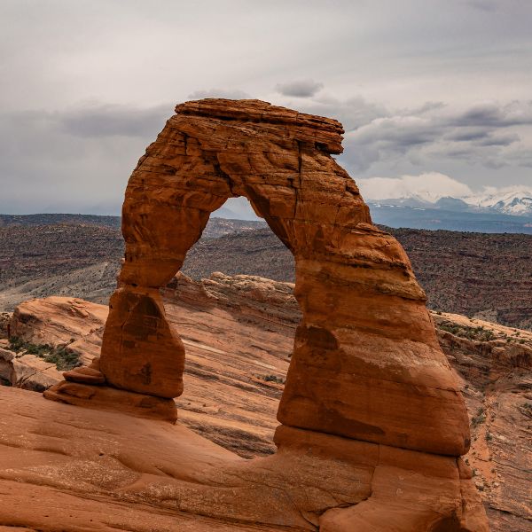 Delicate Arch in Arches National Park stands alone against a backdrop of red rock formations and a cloudy sky, capturing the park’s iconic desert landscape.