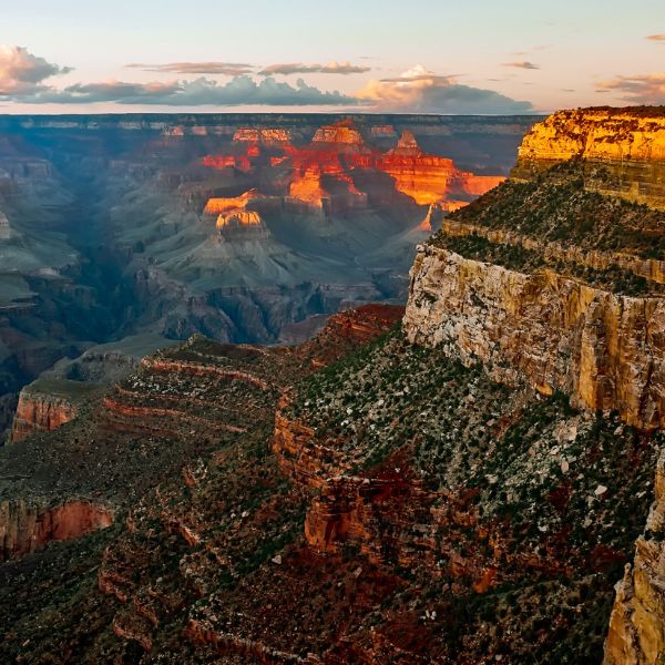 Layers of massive red rock cliffs and deep valleys stretch across the iconic Grand Canyon landscape, glowing in warm sunset light.