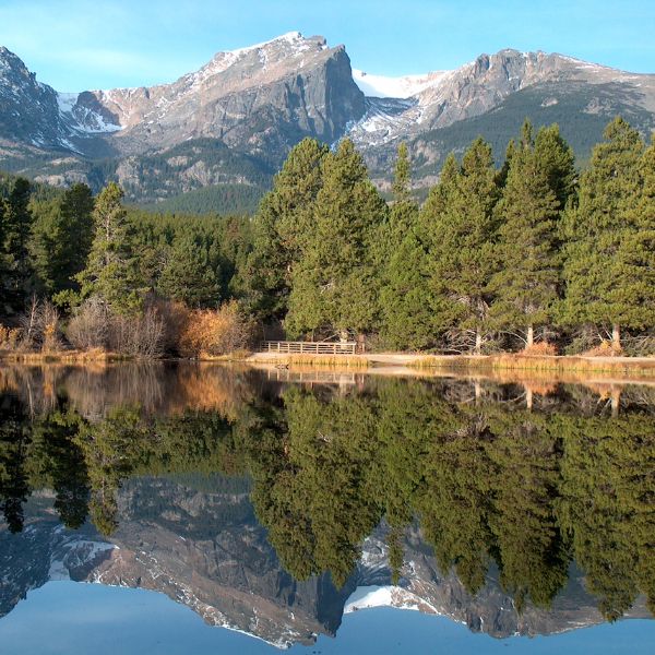 Scenic view of Rocky Mountain National Park with snow-capped peaks and a dense forest reflecting in a still lake