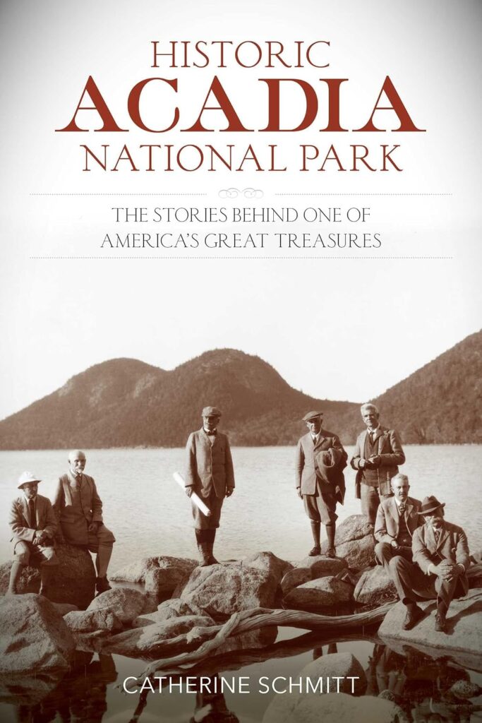Book cover of "Historic Acadia National Park. The Stories Behind One of America's Great Treasures" by Catherine Schmitt. A sepia toned historical photograph shows seven men in suits posing on shoreline rocks beside a lake with forested mountains in the background.