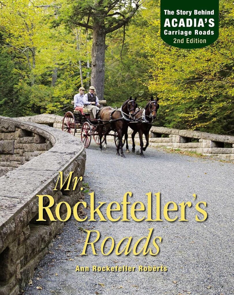 Book cover of "Mr. Rockefeller's Roads" by Ann Rockefeller Roberts, with the subtitle "The Story Behind Acadia's Carriage Roads. 2nd Edition." Two people ride in a horse drawn carriage pulled by two brown horses across a curved stone bridge surrounded by trees with yellow and green autumn foliage.